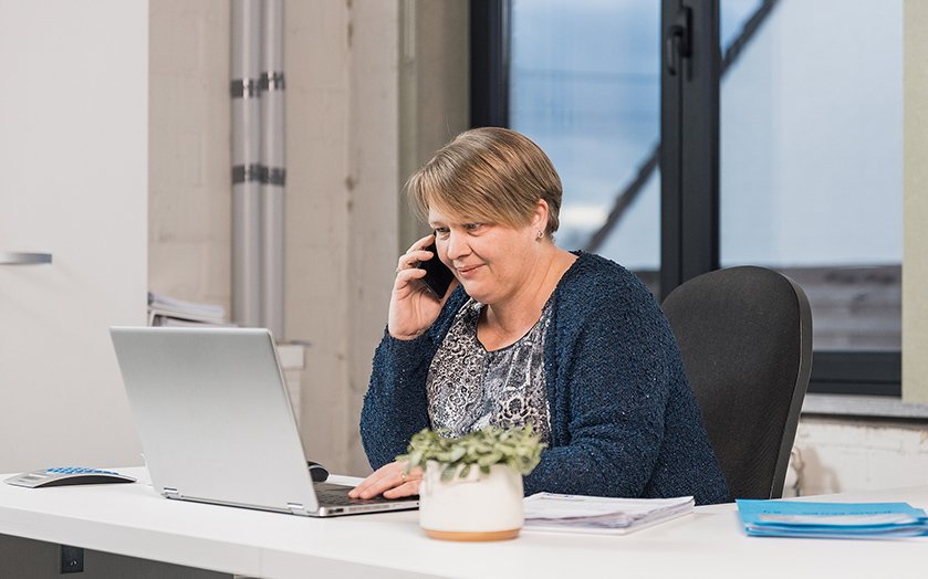 Vrouw aan bureau belt en werkt op laptop in kantooromgeving van De Woonwaaier renovatiepartner