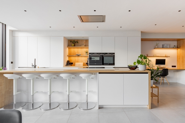 Moderne open keuken met wit eiland, barkrukken en geïntegreerde oven in een strak gerenoveerde woning