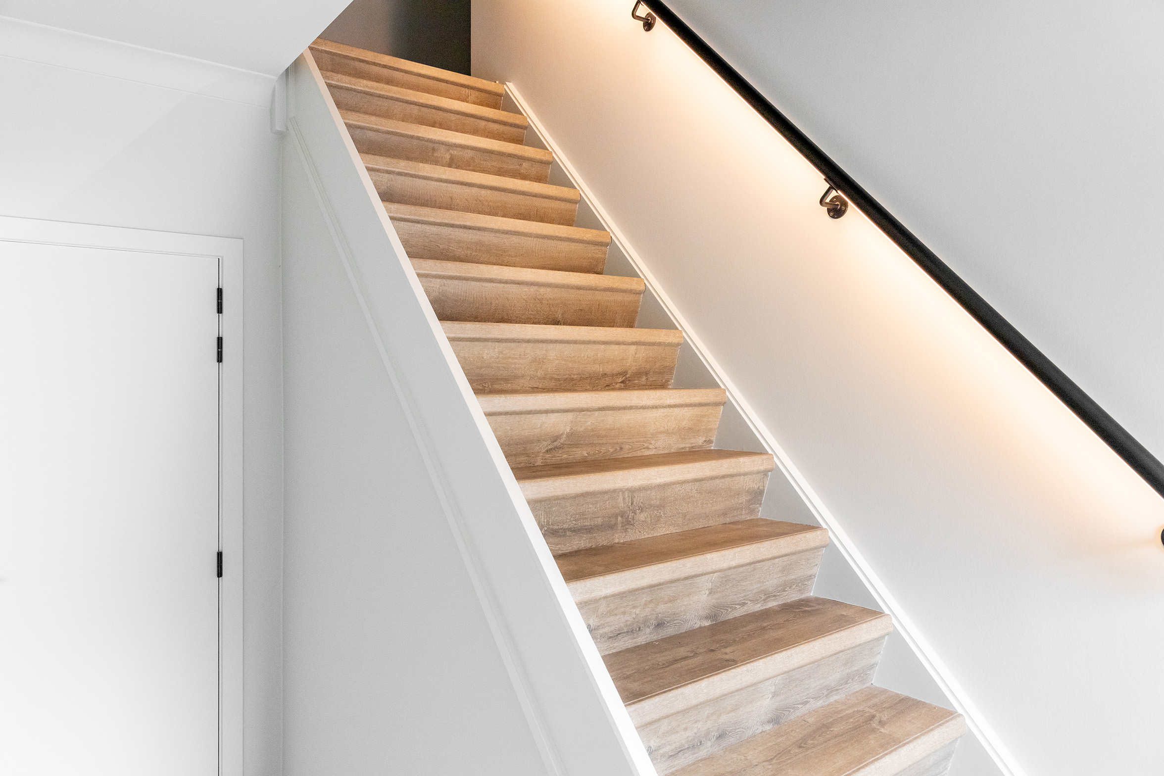Moderne houten trap met witte wanden en ingebouwde handrail verlichting in woning renovatie