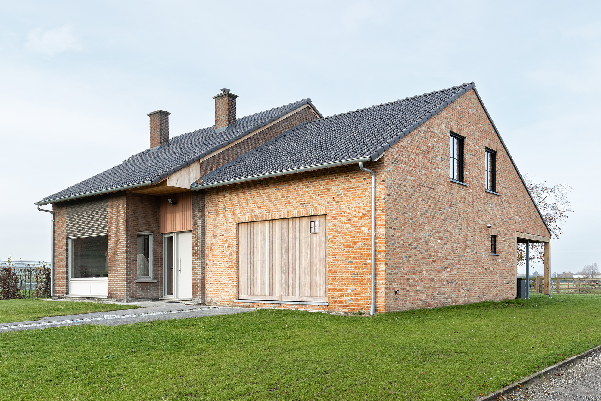 Modern gerenoveerde woning met bakstenen gevel, houten garagepoort en grijze dakpannen omgeven door groen gazon