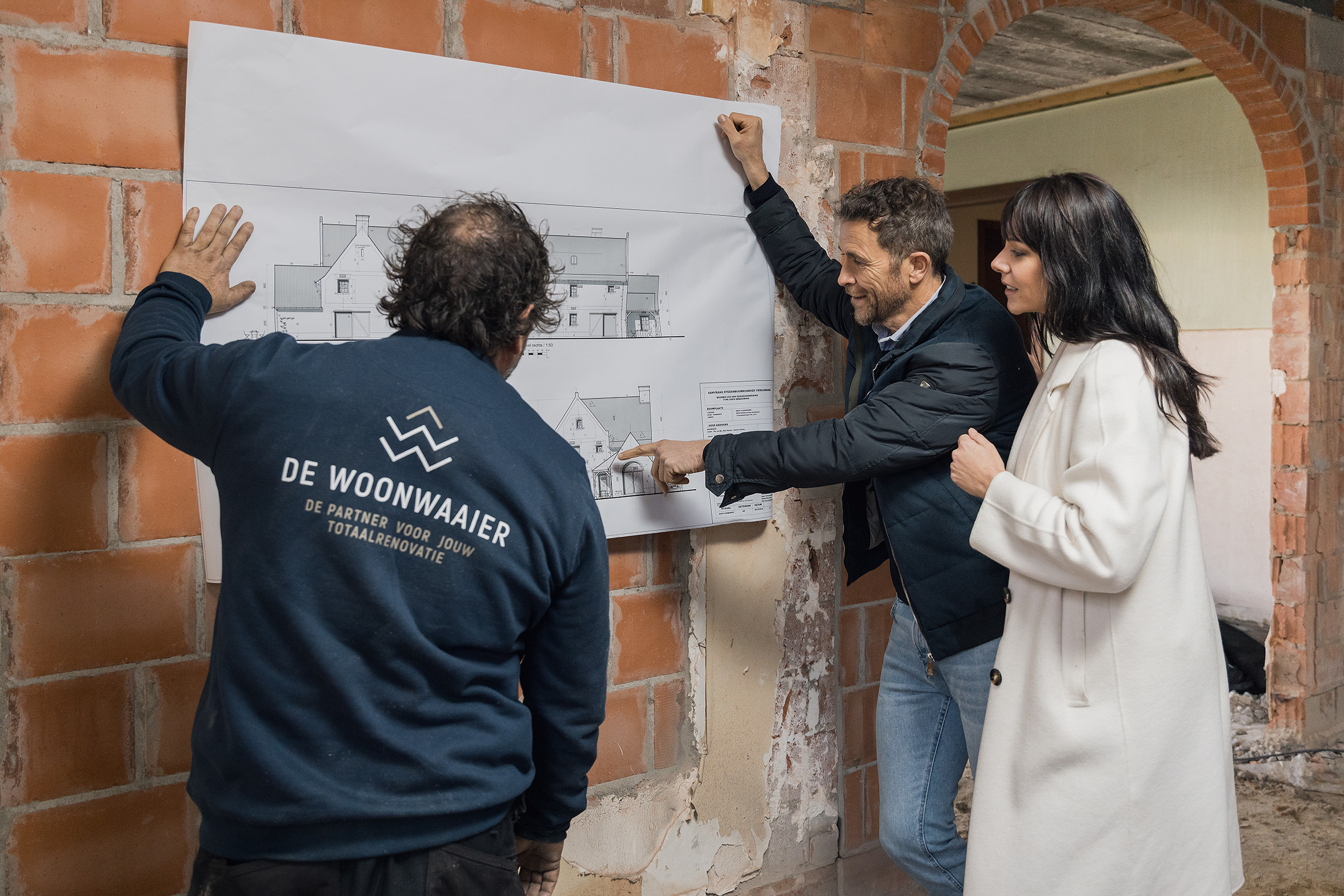 Drie mensen bespreken plattegrond in een woningonderhoud project met zichtbare bakstenen en ruwe afwerking