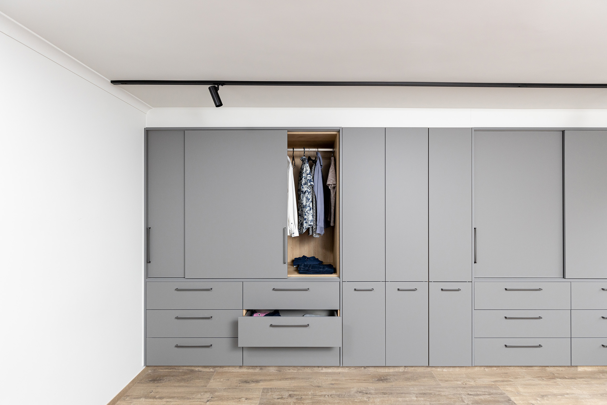 Strakke grijze ingebouwde kasten met open deur en lade in modern interieur