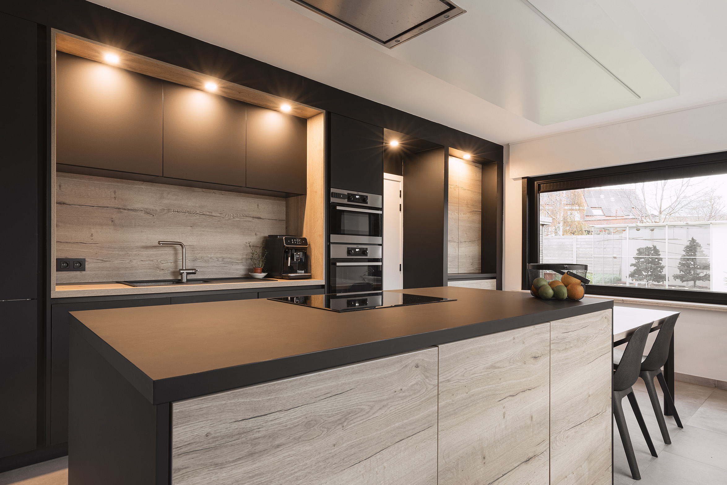Moderne keuken met houten accenten, ingebouwde oven, kookplaat en groot raam met uitzicht op tuin