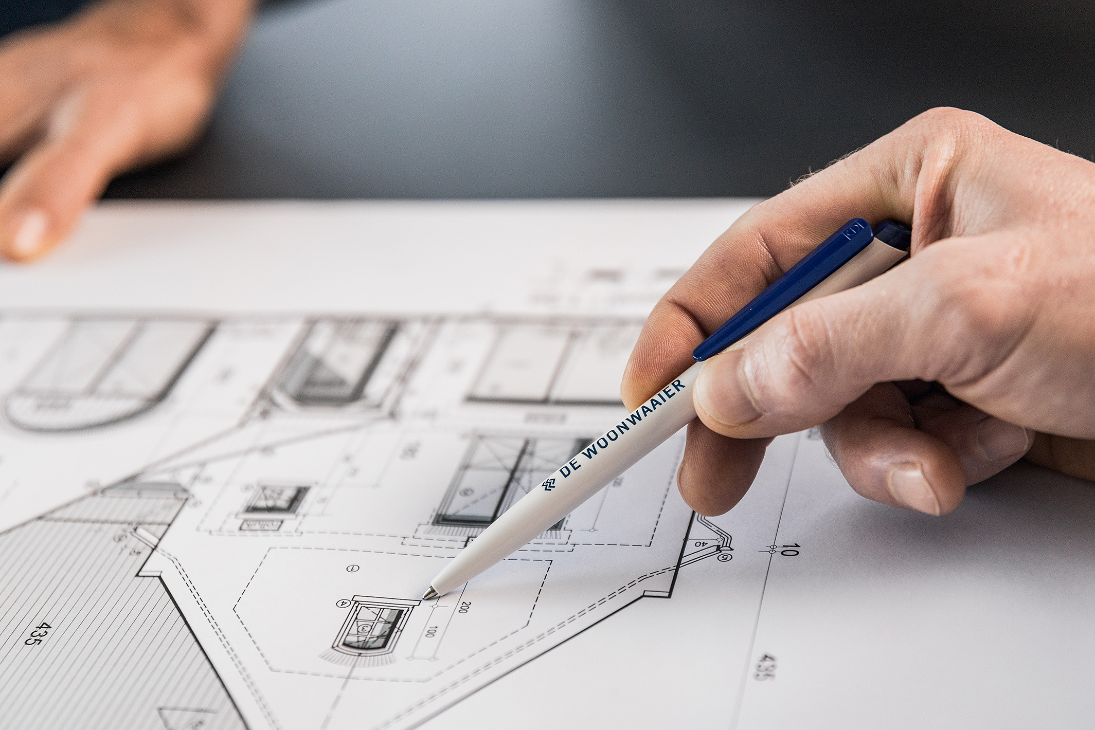 Hand met pen van De Woonwaaier wijzend op bouwplan van woning renovatie project