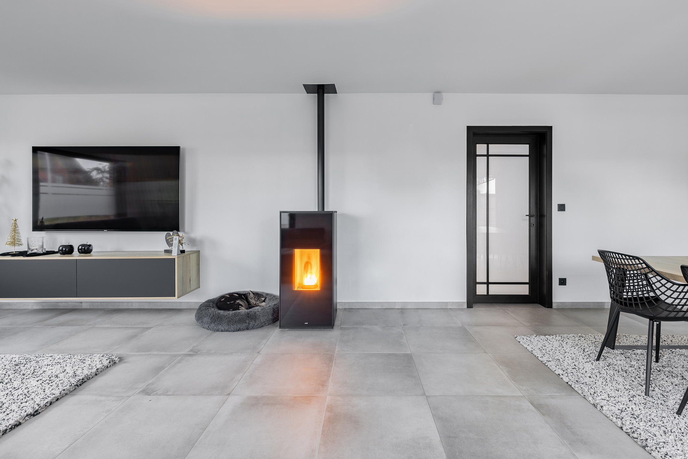 Moderne woonkamer met ingebouwde haard, grijze tv-meubel, zwarte deur en kat op zacht kussen